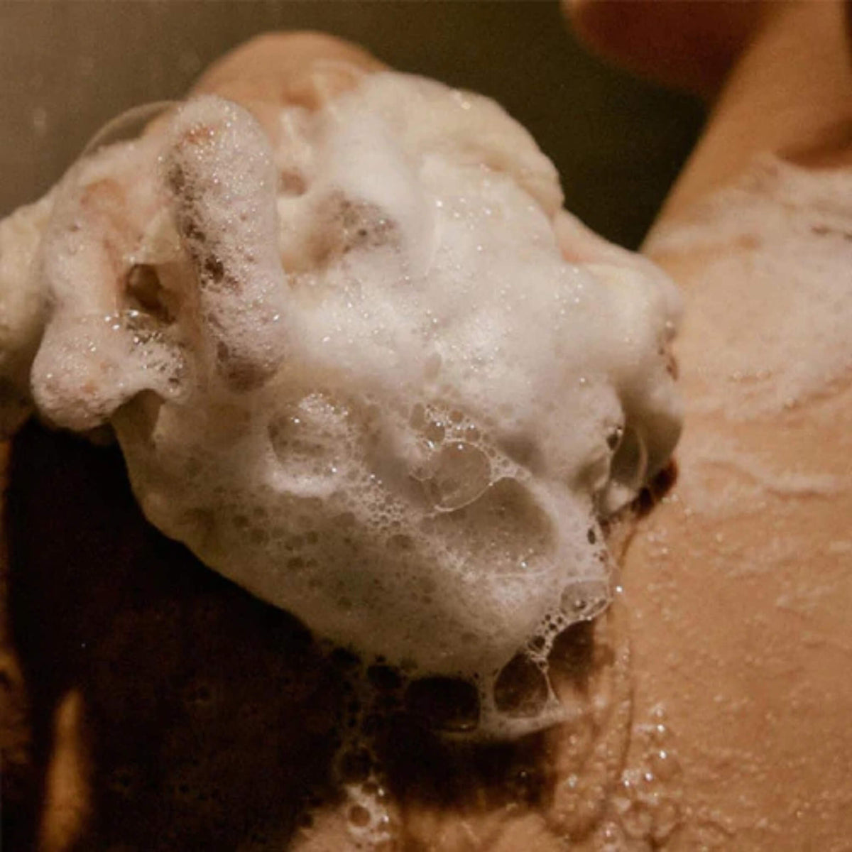 Close-up of a hand with soap suds on a brown background