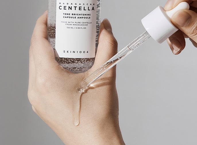Hand holding a skincare bottle with a dropper, featuring Skinfood product on a neutral background