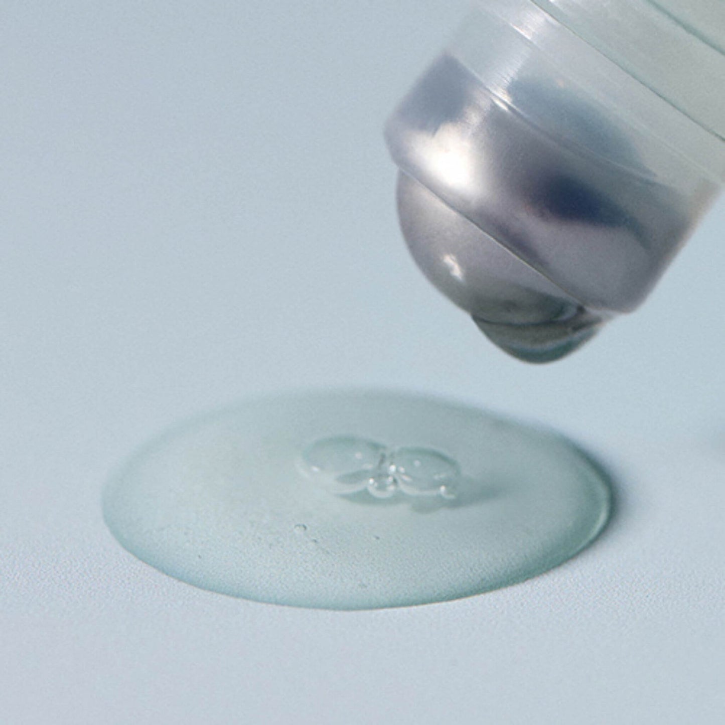 Clear liquid being dispensed from a silver bottle onto a light blue surface.