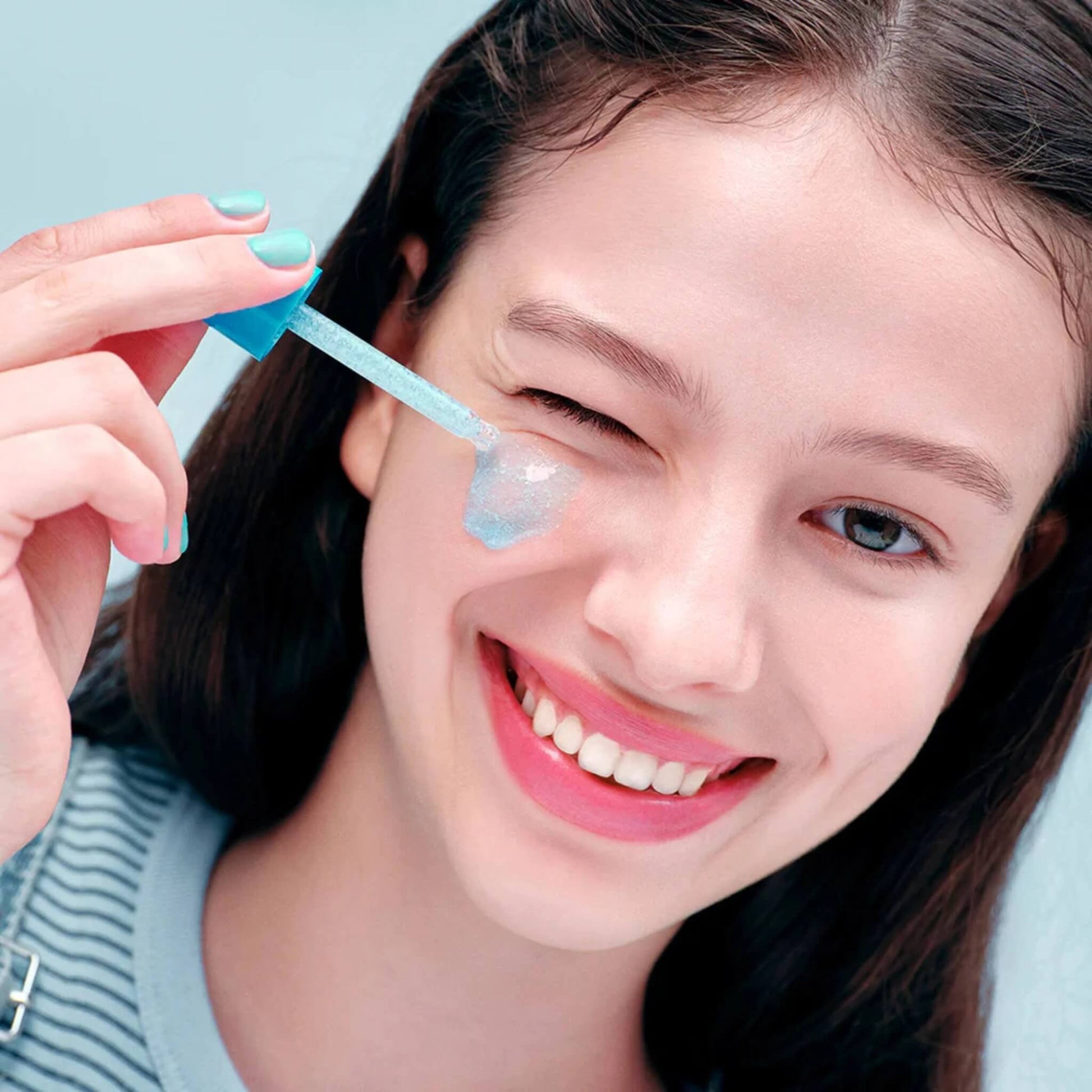 Woman using a skincare product on her face with a blue background