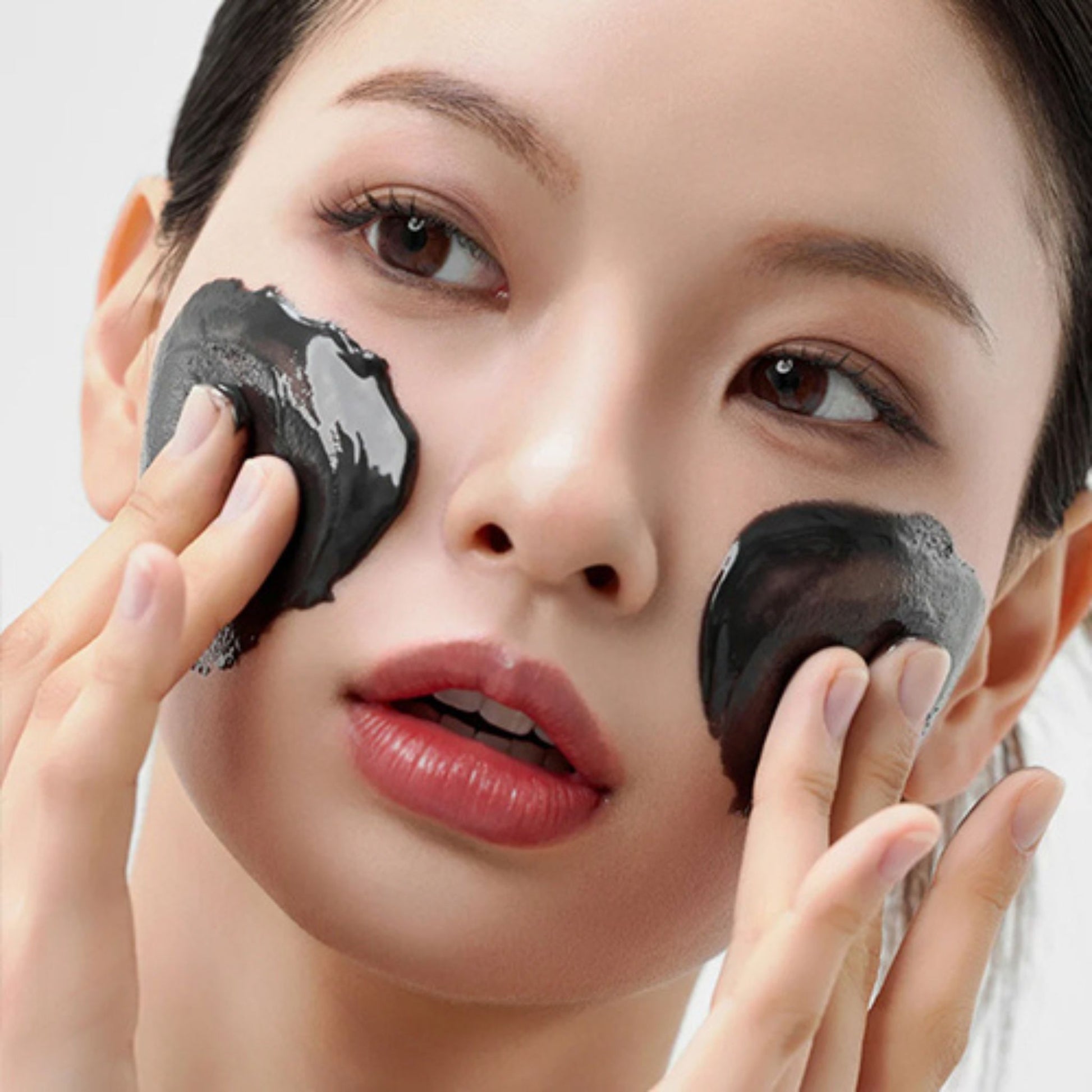 Woman applying black facial mask to her face