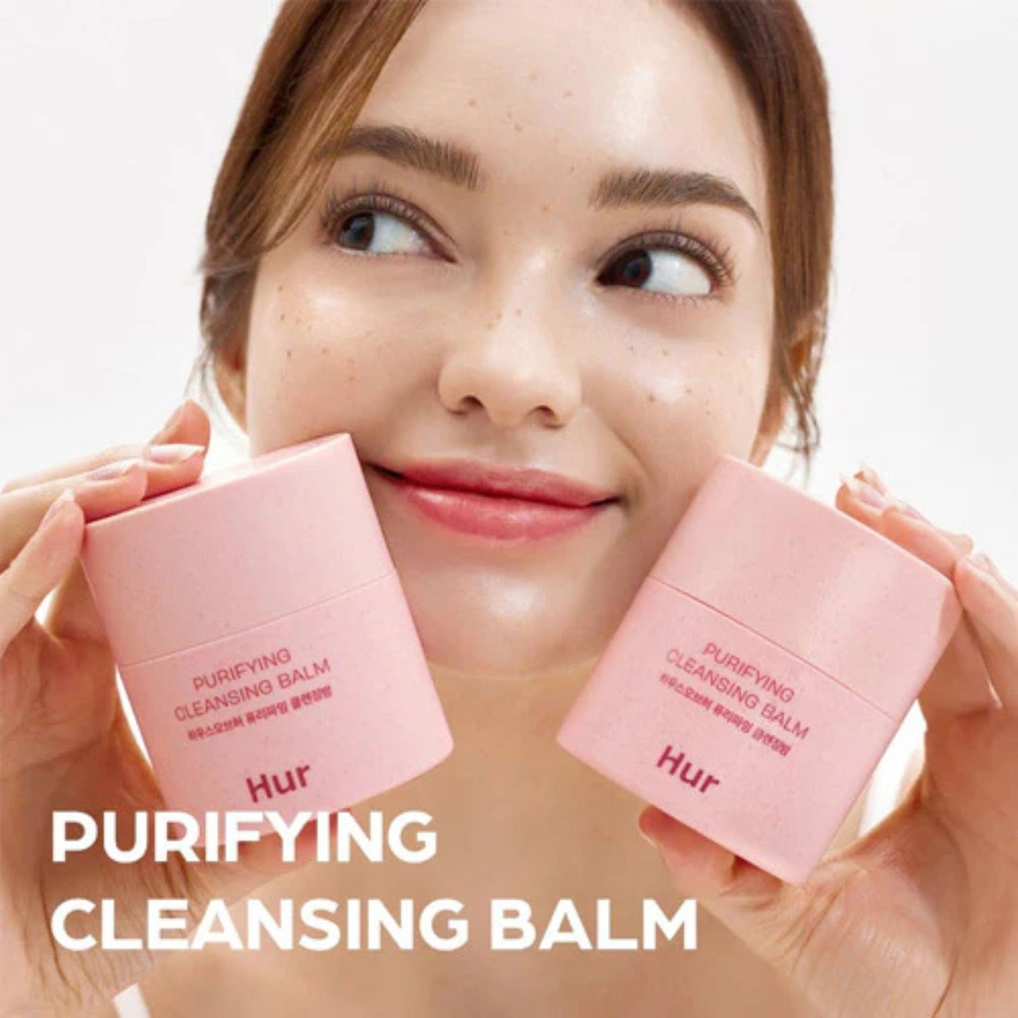 Woman holding pink 'HUR' cleansing balms with a blurred background