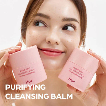 Woman holding pink 'HUR' cleansing balms with a blurred background