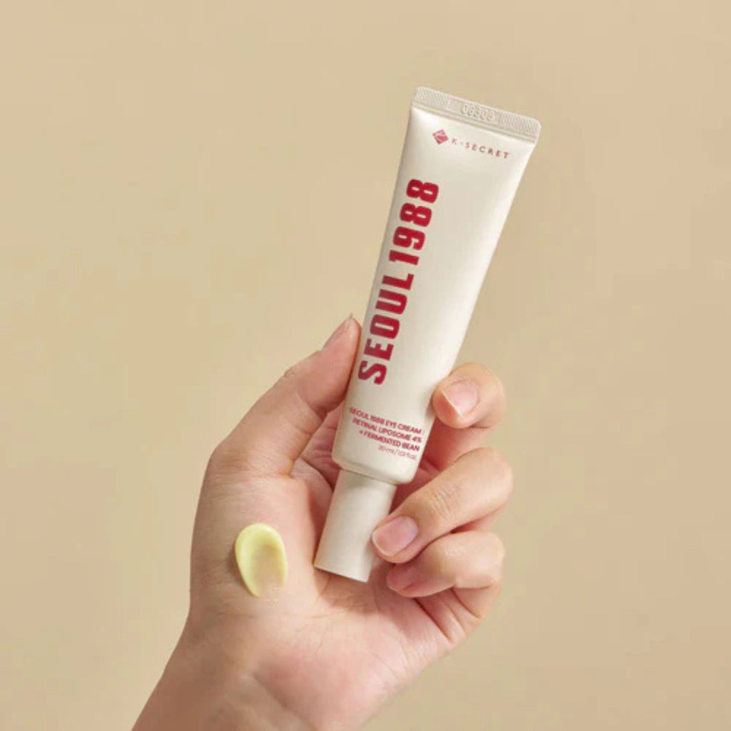 Hand holding a tube of 'Seoul 1988' cream against a beige background