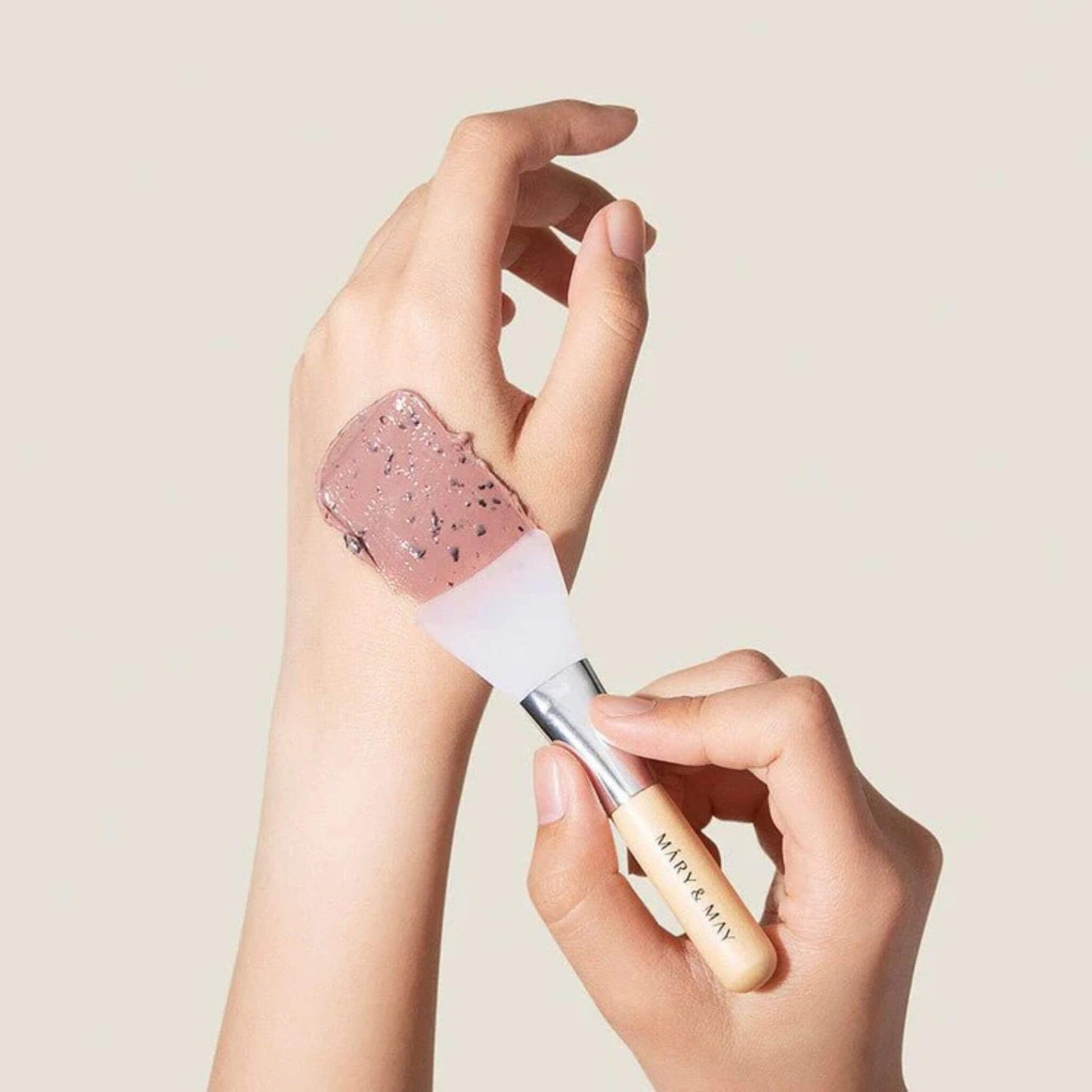 Hand applying glittery pink makeup to wrist with a brush