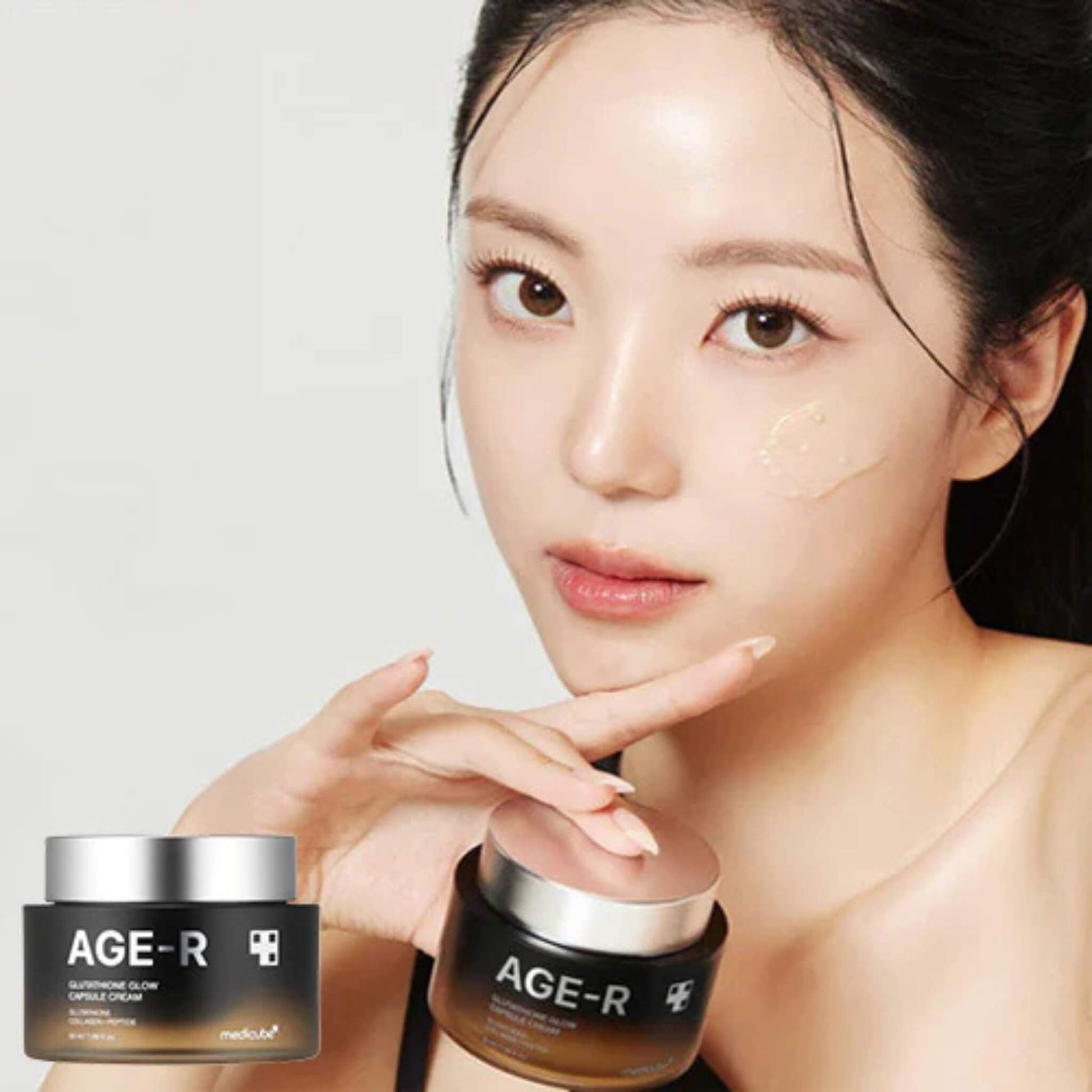 Woman holding two jars of AGE-R skincare product against a white background