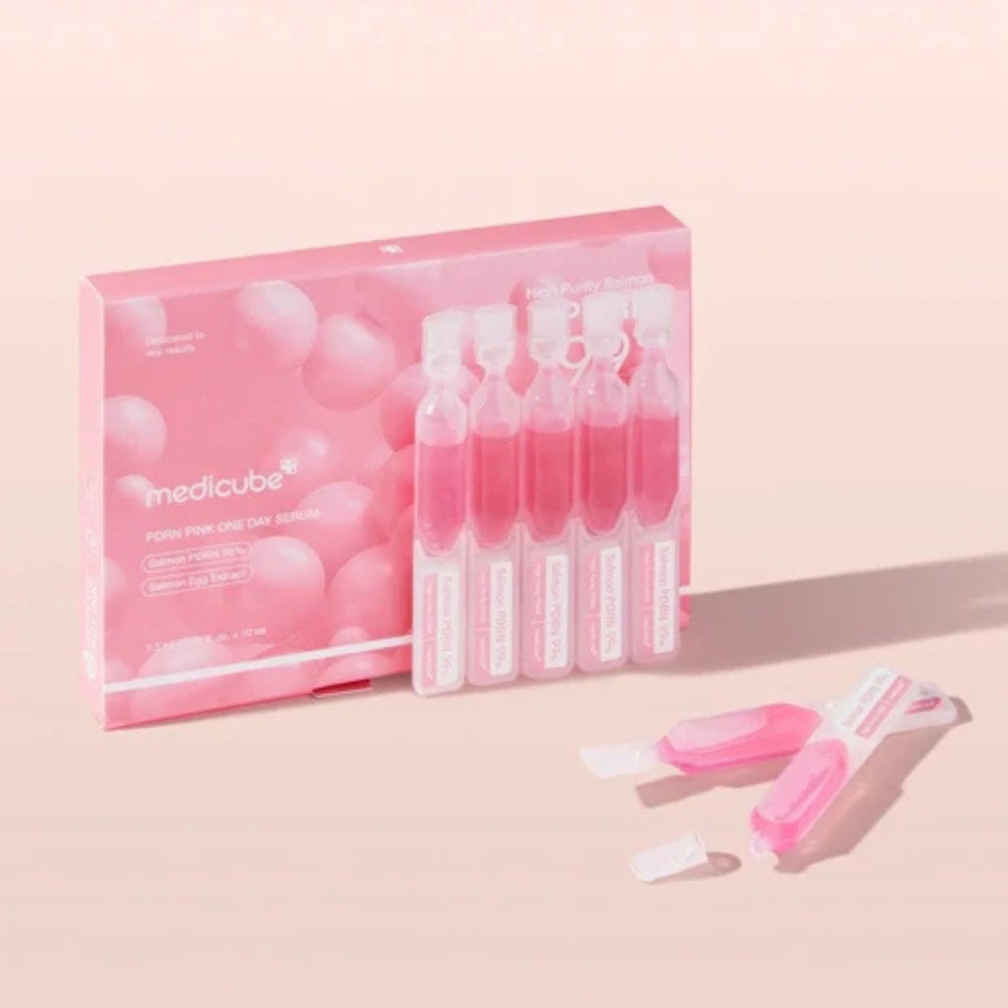 Pink packaging of Medicube face serum with serum bottles on a light pink background