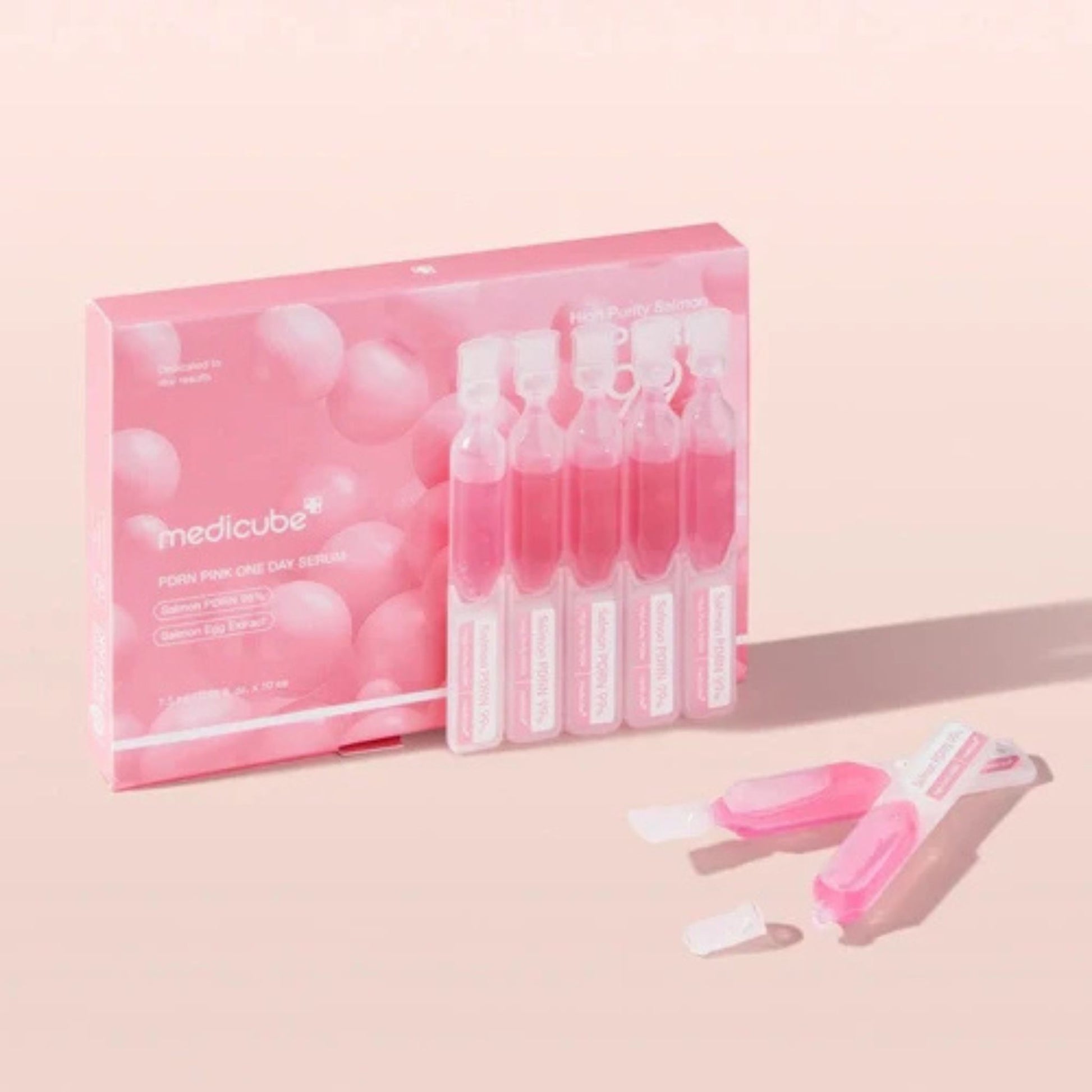 Pink packaging of Medicube face serum with serum bottles on a light pink background