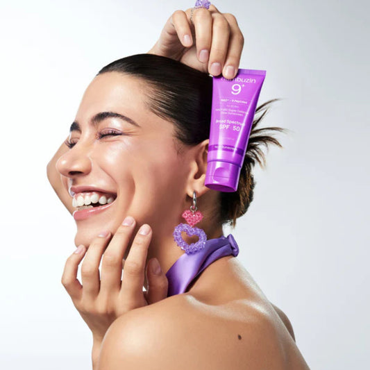 Woman applying purple sunscreen to her face with a white background