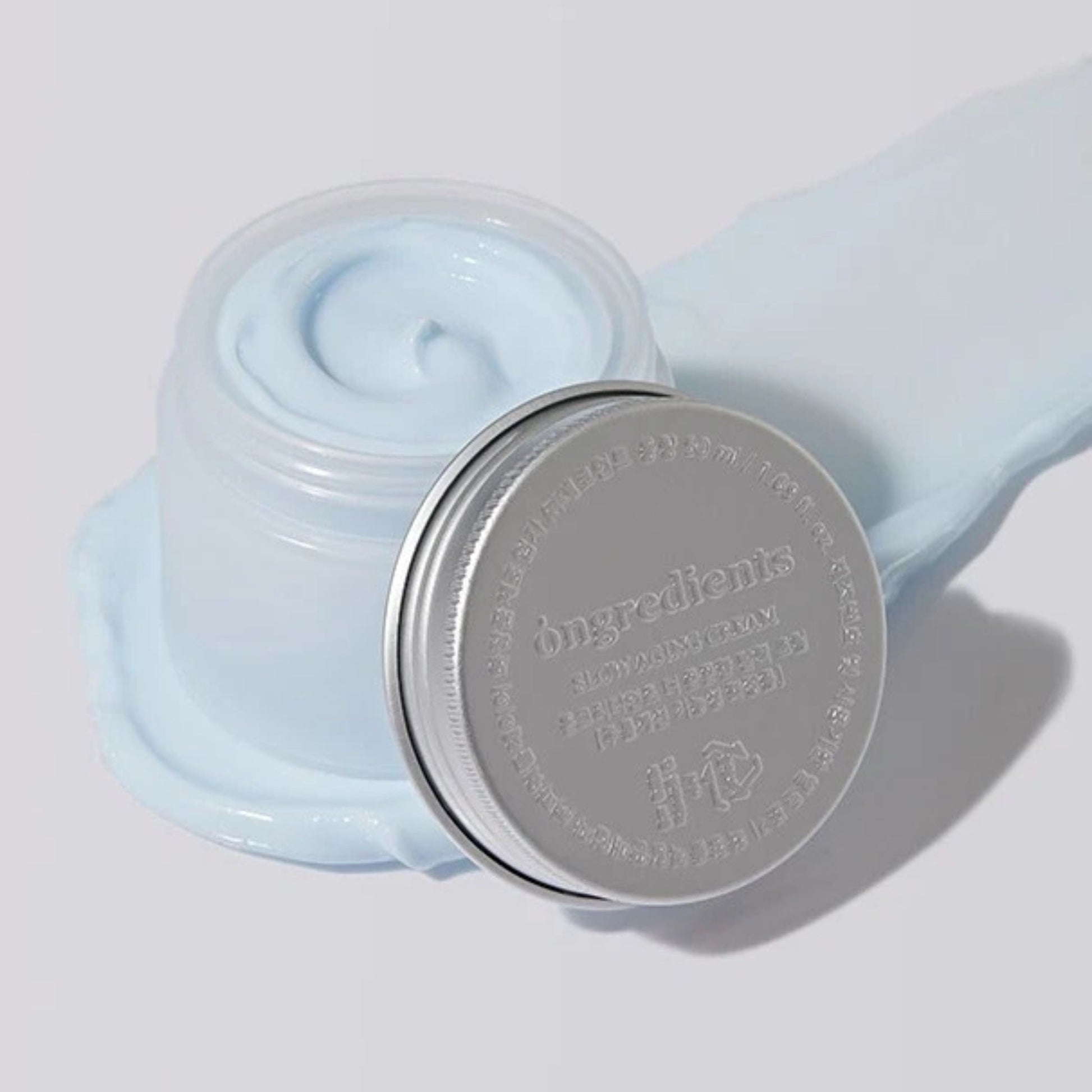 Jar of light blue cream with a silver lid on a white background