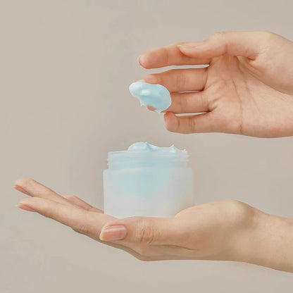 Hand holding a small container of light blue cream against a neutral background