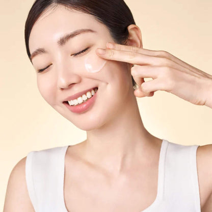 Woman applying cream to her face with a beige background
