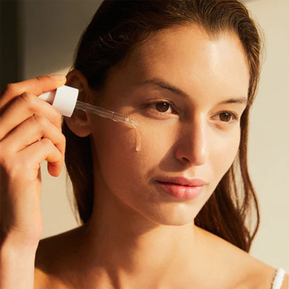 Woman applying a dropper of skincare product to her face.