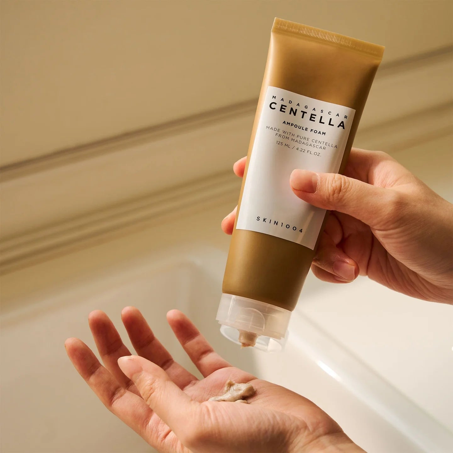 Hand holding a Skintoo tube of Madagascan Centella Astringent Foam with a beige background