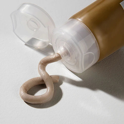 Cosmetic tube with beige cream being squeezed out on a light background