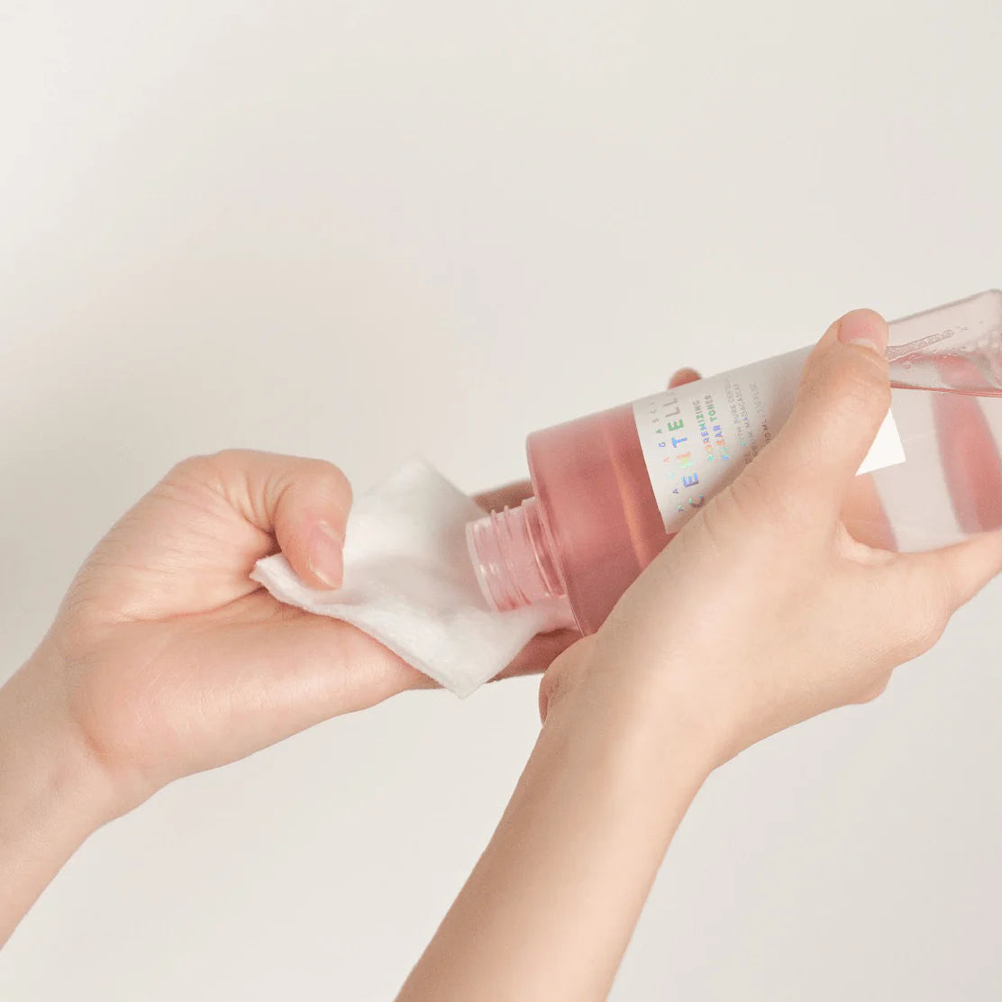 Person holding a pink bottle with a white cap against a light gray background