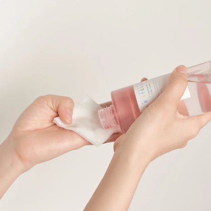 Person holding a pink bottle with a white cap against a light gray background