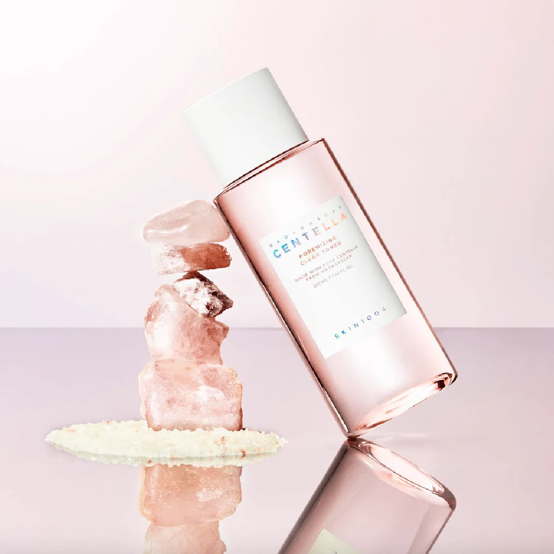 Rose gold skincare bottle with a white cap on a light pink background