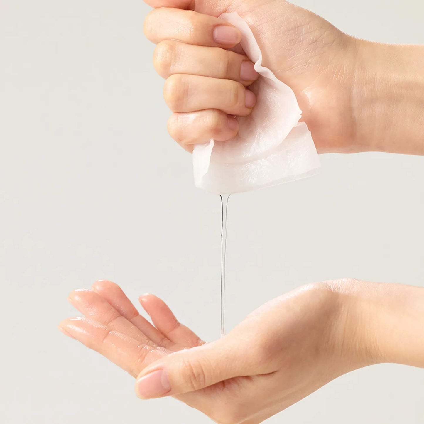 Hand squeezing a white tube of cream onto another hand against a light gray background