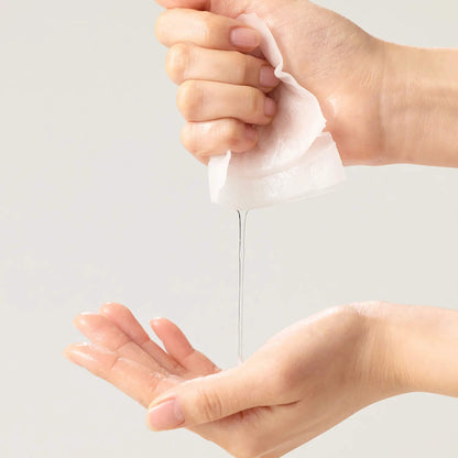 Hand squeezing a white tube of cream onto another hand against a light gray background