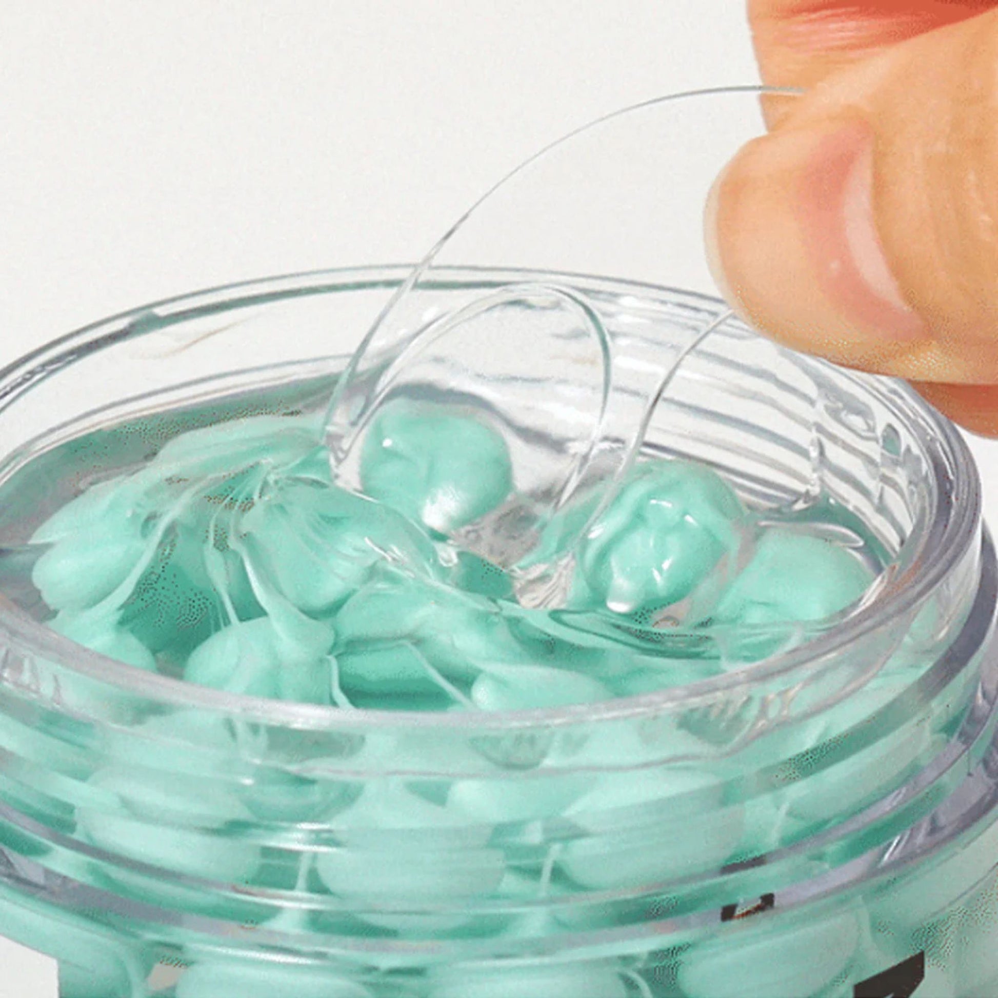 Clear container with green gel-like substance and a hand holding the lid.